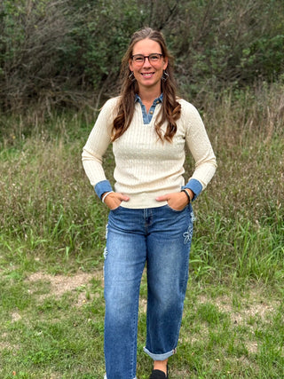 A lady wearing a ivory cable knit sweater with denim trim on the collar and sleeves.