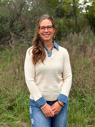 A lady wearing a ivory cable knit sweater with denim trim on the collar and sleeves.