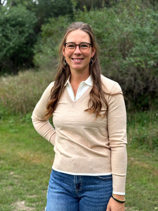 A lady wearing an oatmeal sweater with a 1/4 zip up with ivory trim detail.