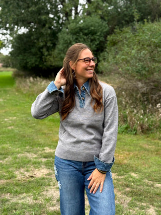 A lady wearing a grey sweater with denim trim around the collar and cuffs.