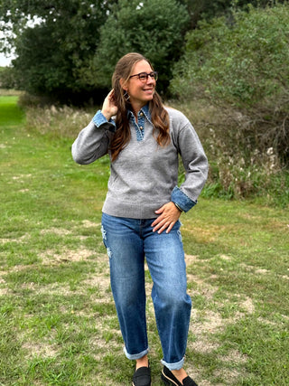 A lady wearing a grey sweater with denim trim around the collar and cuffs.
