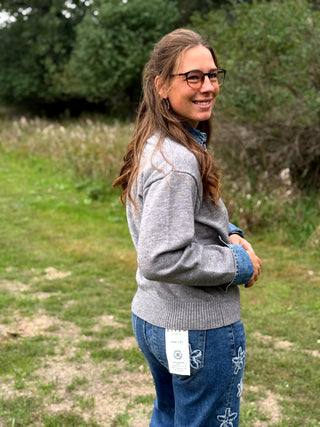 A lady wearing a grey sweater with denim trim around the collar and cuffs.