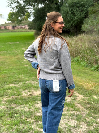 A lady wearing a grey sweater with denim trim around the collar and cuffs.