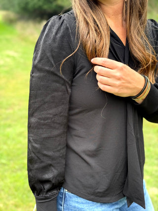 A lady wearing a black top with a scarf and gold detail.