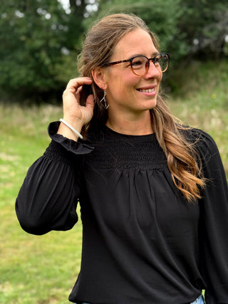 A lady wearing a black top with smocking detail.