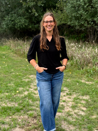 A lady wearing a 3/4 sleeve black top with shoulder detail.