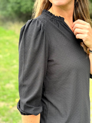 A lady wearing a 3/4 sleeve black top with shoulder detail.