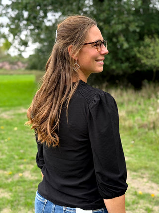A lady wearing a 3/4 sleeve black top with shoulder detail.