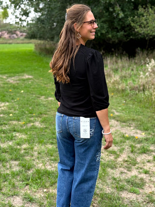 A lady wearing a 3/4 sleeve black top with shoulder detail.