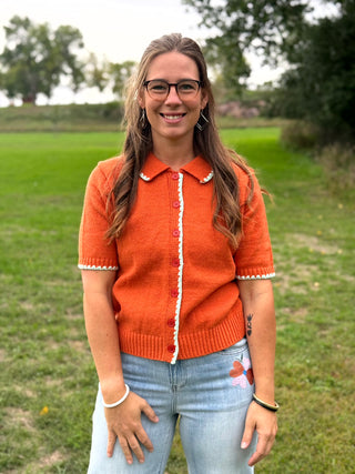 A lady wearing a orange short sleeve button up cardigan with whip stitch detail.