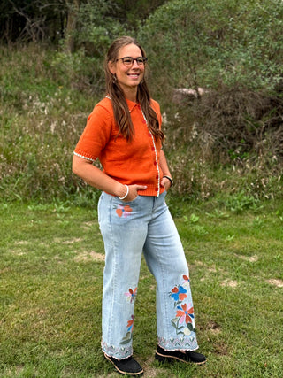 A lady wearing a light colored jeans with colorful embroidery on them.