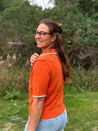 A lady wearing a orange short sleeve button up cardigan with whip stitch detail.