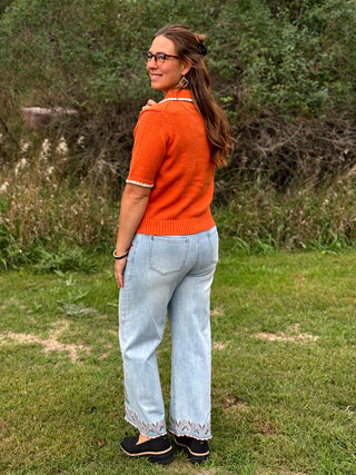A lady wearing a light colored jeans with colorful embroidery on them.