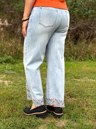 A lady wearing a light colored jeans with colorful embroidery on them.