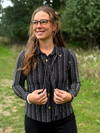 A lady wearing a black and white pin stripe blouse with a scarf detail.