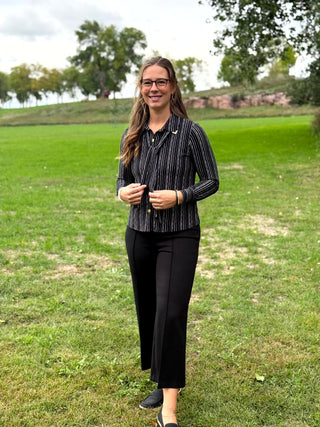 A lady wearing a black and white pin stripe blouse with a scarf detail.