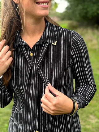 A lady wearing a black and white pin stripe blouse with a scarf detail.