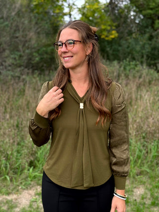 A lady wearing a olive green top with a scarf detail.