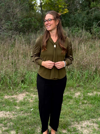 A lady wearing a olive green top with a scarf detail.
