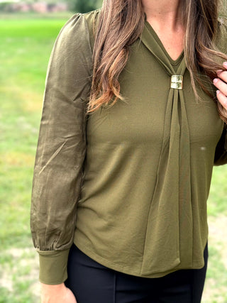 A lady wearing a olive green top with a scarf detail.