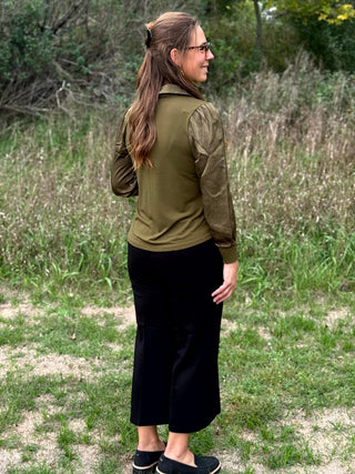 A lady wearing a olive green top with a scarf detail.