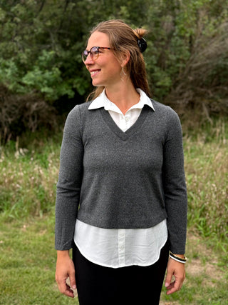 A lady wearing a long sleeve charcoal sweater with a white 2-fer look.