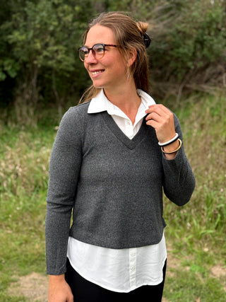 A lady wearing a long sleeve charcoal sweater with a white 2-fer look.
