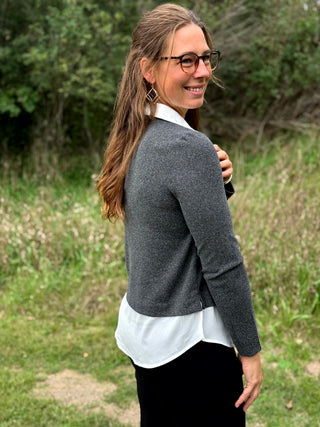 A lady wearing a long sleeve charcoal sweater with a white 2-fer look.