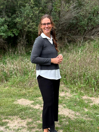 A lady wearing a long sleeve charcoal sweater with a white 2-fer look.