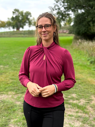 A woman wearing a long-sleeve burgundy mock neck blouse and black wide-leg pants, standing outdoors on a grassy field.