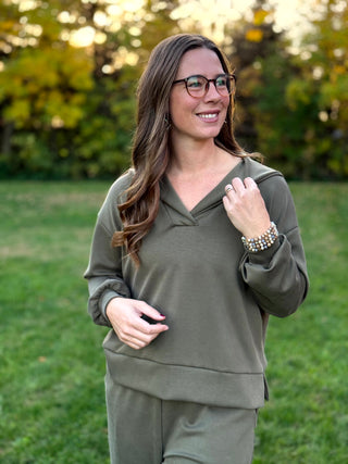 Model wearing an olive green collared V-neck pullover with relaxed long sleeves and a banded hem.