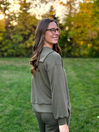 Side-back view of an olive green pullover showing the wide collar, dropped shoulders, and fitted cuffs.