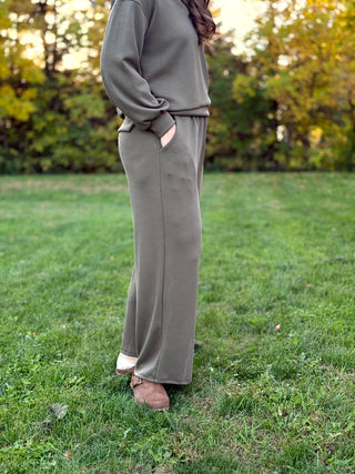 Side view of olive green wide-leg pants, showing a side pocket with the model’s hand tucked inside.
