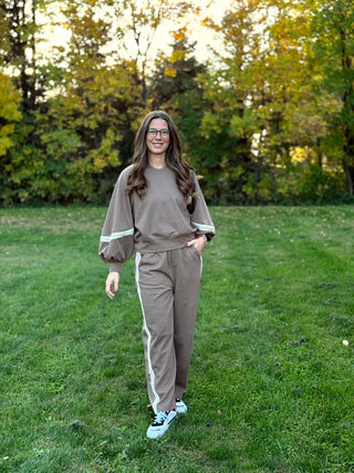 Full-length view of a model wearing a taupe matching set with cream lace sleeve accents and pant side stripes.