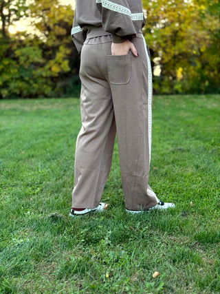 Rear view of taupe pants showing an elastic waistband, back patch pocket, and cream lace side trim.