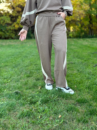 Front view of taupe relaxed-fit pants with cream lace side stripes, styled with a matching balloon-sleeve top.