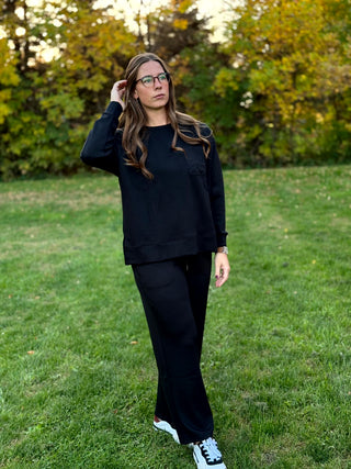 Front view of model wearing a black long-sleeve chest-pocket top and matching wide-leg pants with white sneakers.