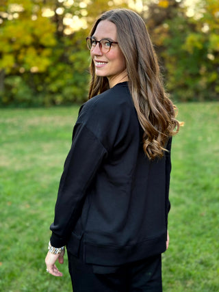 Back view of a black relaxed-fit top showing dropped shoulders and a wide hem with side slits.