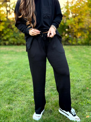 Close-up of black lounge set with a long-sleeve chest-pocket top and wide-leg drawstring pants.