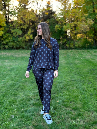 Model wearing a dark charcoal crewneck sweatshirt and matching pants with large gray polka dots, standing outdoors.

