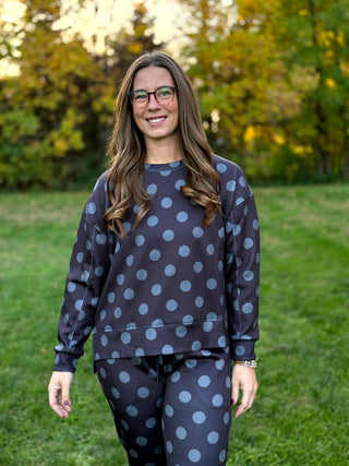 Model wearing a dark charcoal crewneck sweatshirt and matching pants with large gray polka dots, standing outdoors.

