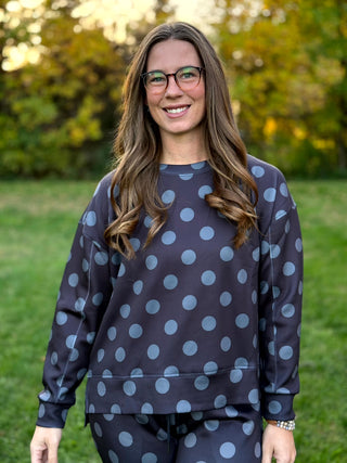 Model wearing a dark charcoal crewneck sweatshirt and matching pants with large gray polka dots, standing outdoors.

