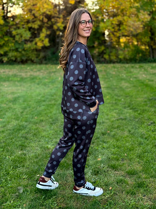 Model wearing a dark matching sweatshirt and jogger set with gray polka dots, shown from the side with one hand in a pocket.