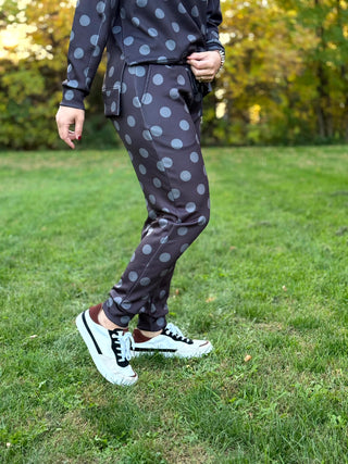 Model wearing dark charcoal jogger pants with large gray polka dots, paired with black-and-white sneakers.