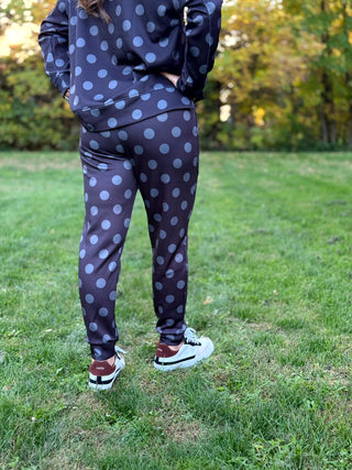 Rear view of a model wearing a dark sweatshirt and matching gray polka-dot joggers with cuffed ankles and white sneakers.