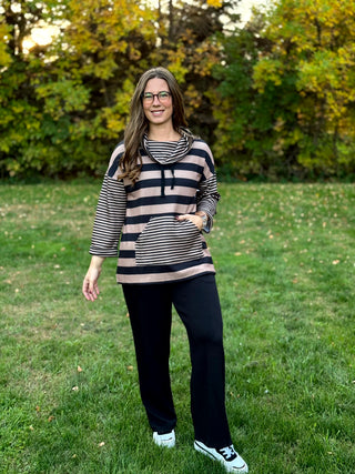 Model wearing a black and taupe striped cowl-neck top with drawstrings, contrasting striped sleeves and kangaroo pocket, paired with black pants.⠋