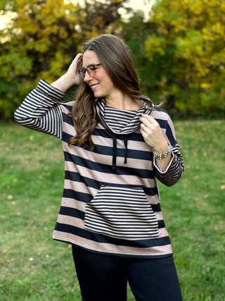 Model wearing a black and taupe striped pullover, showing the drawstring cowl neck and contrasting narrow-striped kangaroo pocket.