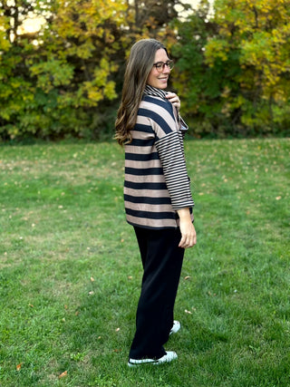 Full-length side view of a model wearing black wide-leg pants with a black and taupe striped top and white sneakers.