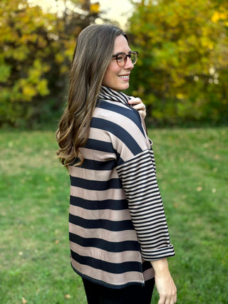 Side and back view of a model wearing a black and taupe wide-striped pullover with contrasting narrow-striped sleeves and cowl neck.