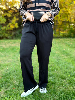 Front view of black wide-leg pants with a drawstring waist and side pockets, modeled with white sneakers.